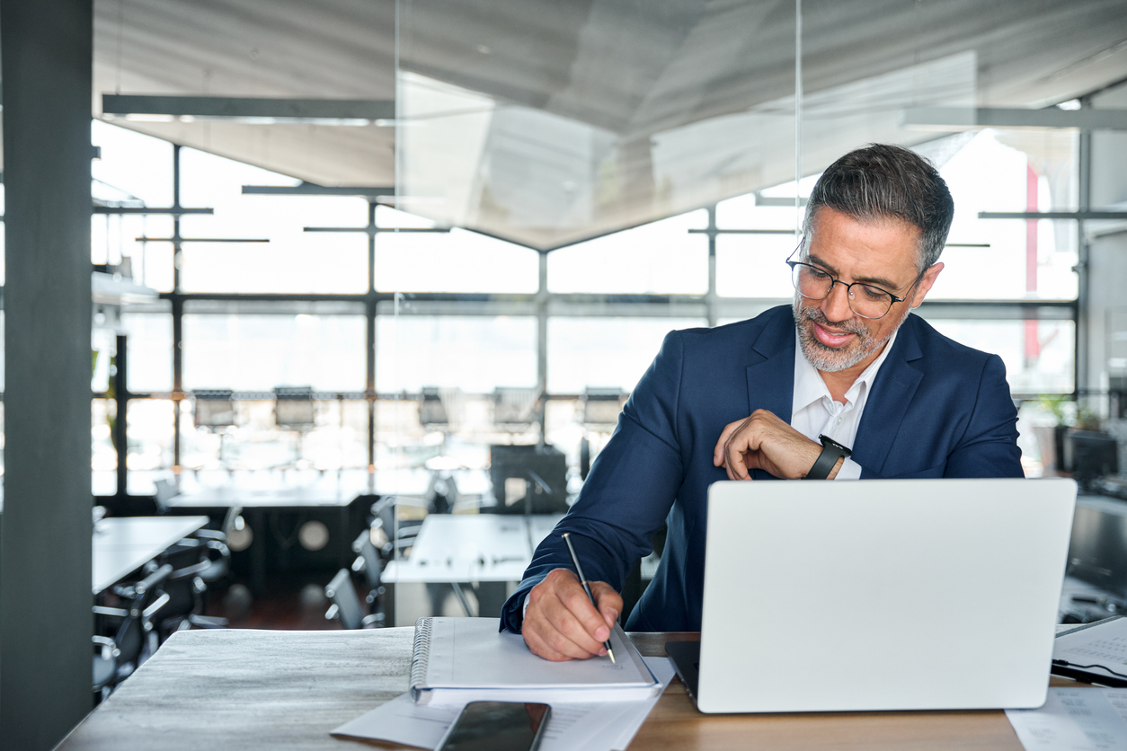 man looking at his computer and taking notes