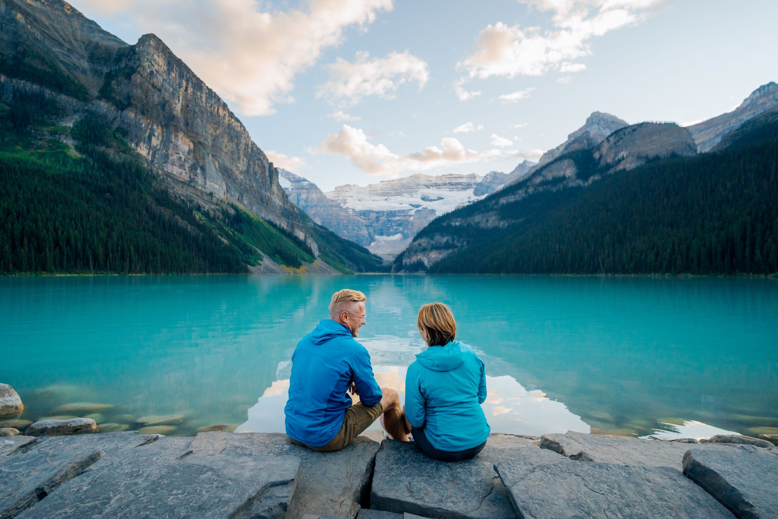 two people sit and admire the view of the lake between two mountains