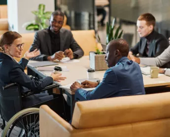 group of coworkers of different ethnicities and abilities chatting in an office setting