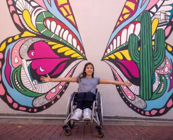 girl in a wheelchair in front of a butterfly mural
