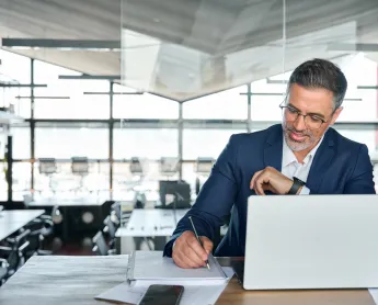 man looking at his computer and taking notes