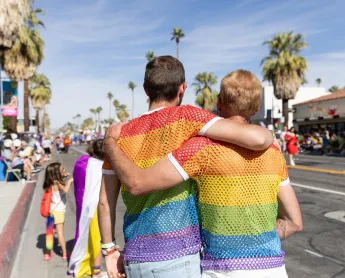 two people embrace while wearing Pride flag shirts