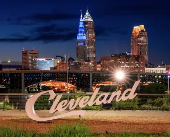 Cleveland sign lit up at night with the city skyline lit up behind it