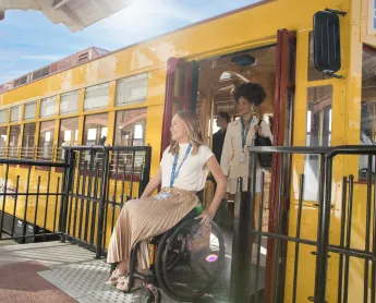 a woman in a wheelchair exits a school bus alongside her friend