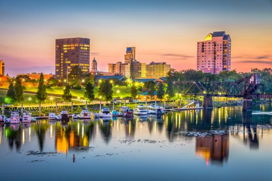 skyline of Augusta, Georgia at sunset. Colorful skies behind tall buildings, trees and water with boats.