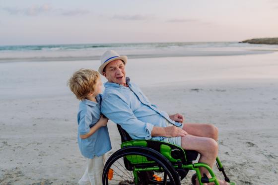 older man in wheelchair on the beach accompanied by a young boy