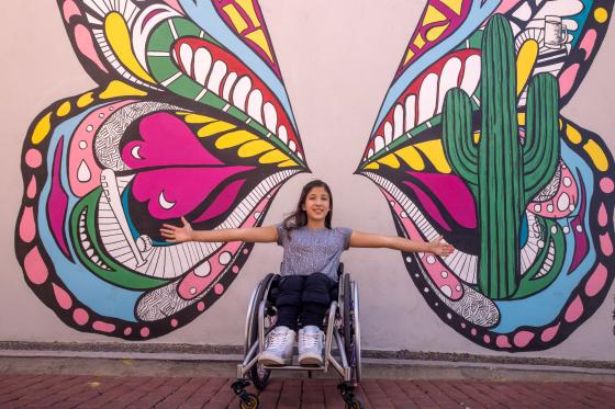 girl in a wheelchair in front of a butterfly mural