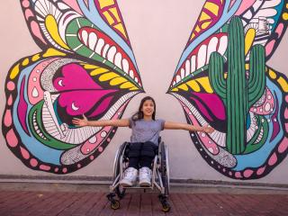 girl in a wheelchair in front of a butterfly mural