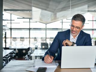 man looking at his computer and taking notes