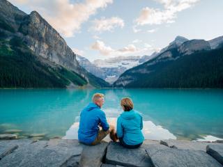two people sit and admire the view of the lake between two mountains