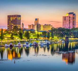 skyline of Augusta, Georgia at sunset. Colorful skies behind tall buildings, trees and water with boats.