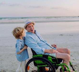 older man in wheelchair on the beach accompanied by a young boy
