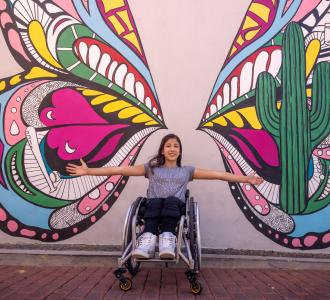 girl in a wheelchair in front of a butterfly mural