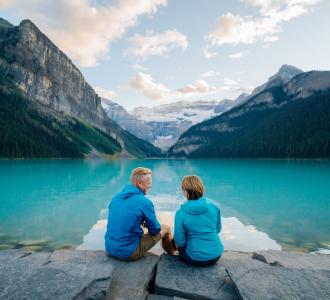 two people sit and admire the view of the lake between two mountains
